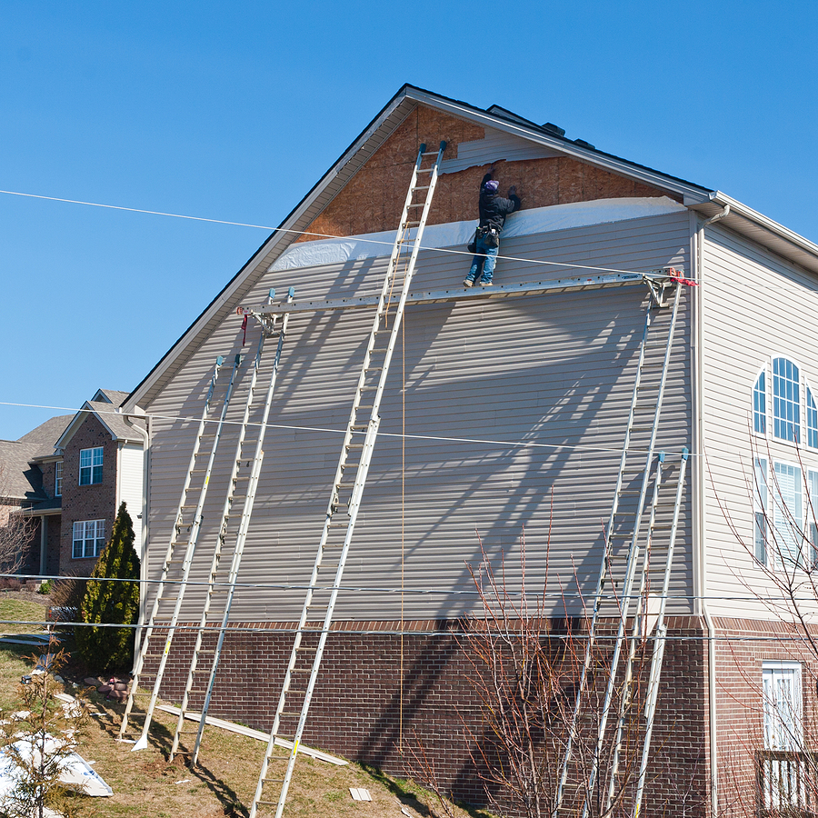 Trusted Siding Installer, Workers installing plastic siding panels on two story house.